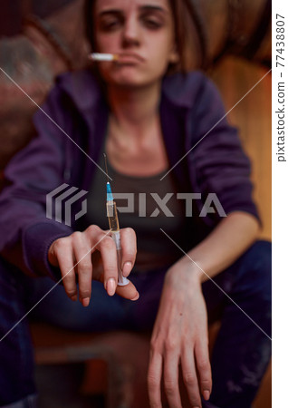 Drug addict female person holds syringe 77438807