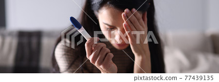 Sad woman sitting on couch and holding pregnancy test closeup Sad woman sitting on couch and holding pregnancy test closeup 77439135