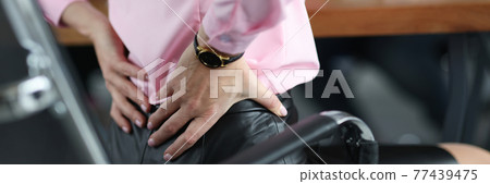 Woman siting on chair in office and holding her lower back closeup Woman siting on chair in office and holding her lower back closeup 77439475