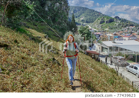 Trekking poles are used by young woman when going uphill. Trekking poles are used by young woman when going uphill. 77439623