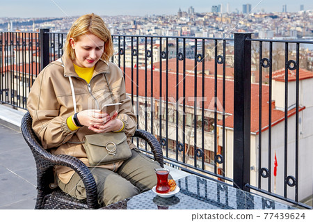 Tea Party on rooftop of hotel overlooking Istanbul cityscape, young woman scans online messages as hot drink cools. Tea Party on rooftop of hotel overlooking Istanbul cityscape, young woman scans online messages as hot drink cools. 77439624