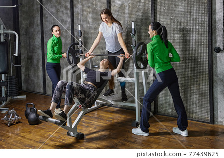 Woman does bench press when others assist her. Woman does bench press when others assist her. 77439625