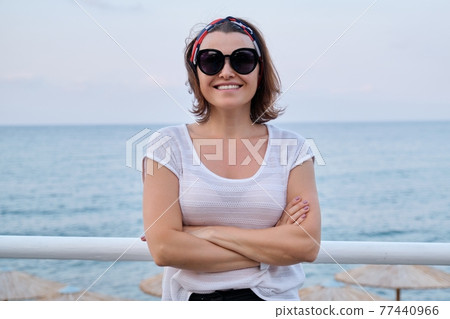 Smiling mature woman in sunglasses looking at camera with crossed arms Smiling mature woman in sunglasses looking at camera with crossed arms 77440966