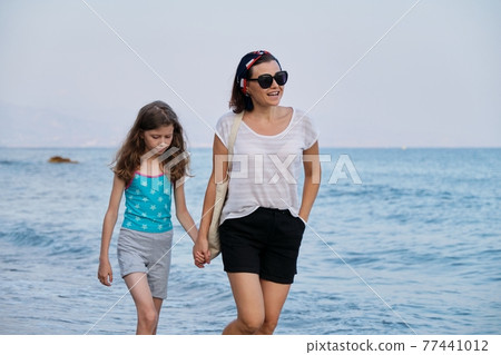 Happy mom and daughter kid walking together on the beach holding hands 77441012
