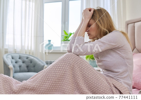 Sad stressful middle-aged woman sitting at home in bed under blanket 77441111