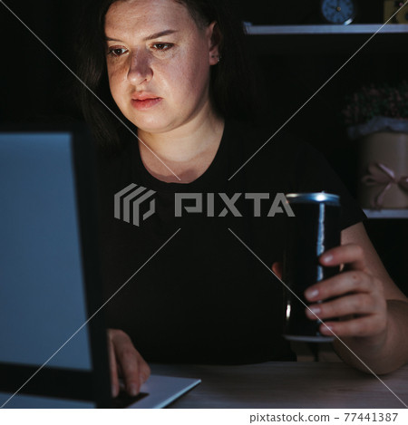 Focused woman drinking energy drink at night Focused woman drinking energy drink at night 77441387
