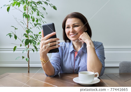 Mature woman with smartphone sitting at home smiling looking at phone screen 77441665