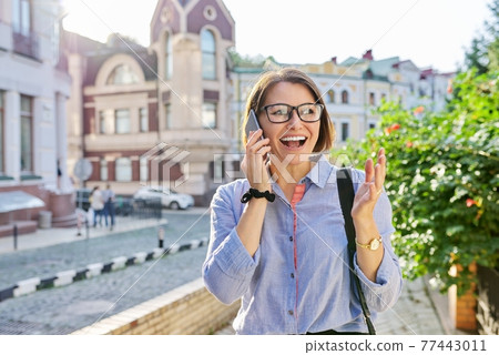 Mature business woman talking on cell phone walking down city street 77443011