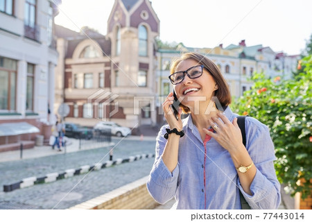 Mature business woman talking on cell phone walking down city street 77443014