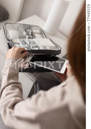 Female hands putting tablet pc into comfortable bag storage get ready to business trip or vacation Female hands putting tablet pc into comfortable bag storage get ready to business trip or vacation 77448329
