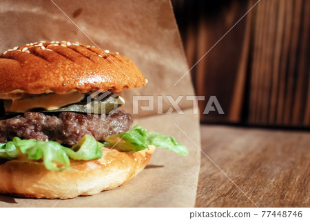 Burger in paper packaging close-up. Food in a fast food restaurant. Macro photo of burger ingredients with meat and vegetables Burger in paper packaging close-up. Food in a fast food restaurant. Macro photo of burger ingredients with meat and vegetables 77448746