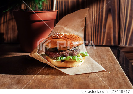 Burger in paper packaging close-up. Food in a fast food restaurant. Macro photo of burger ingredients with meat and vegetables Burger in paper packaging close-up. Food in a fast food restaurant. Macro photo of burger ingredients with meat and vegetables 77448747