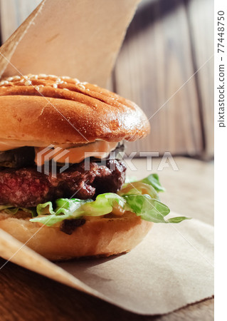 Burger in paper packaging close-up. Food in a fast food restaurant. Macro photo of burger ingredients with meat and vegetables Burger in paper packaging close-up. Food in a fast food restaurant. Macro photo of burger ingredients with meat and vegetables 77448750