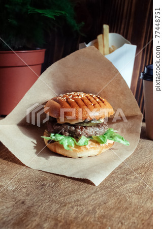 Burger in paper packaging close-up. Food in a fast food restaurant. Macro photo of burger ingredients with meat and vegetables 77448751