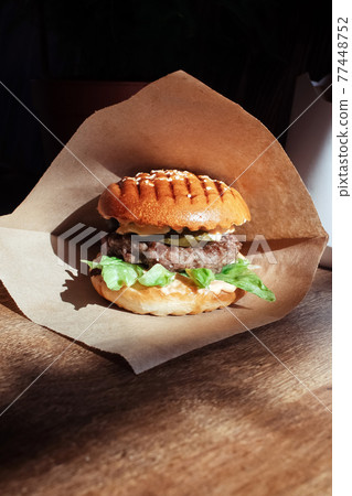 Burger in paper packaging close-up. Food in a fast food restaurant. Macro photo of burger ingredients with meat and vegetables 77448752