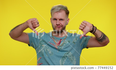 Upset man in fashionable t-shirt showing thumbs down sign gesture, disapproval, dissatisfied dislike 77449152