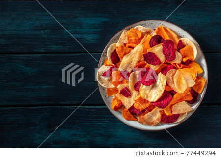 Vegetable chips, shot from above on a dark wooden background Vegetable chips, shot from above on a dark wooden background 77449294