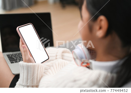 Close up over shoulder view of young girl using smart phone on sofa. Close up over shoulder view of young girl using smart phone on sofa. 77449452