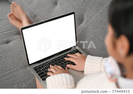 View over shoulder view of young woman using laptop on sofa. View over shoulder view of young woman using laptop on sofa. 77449453