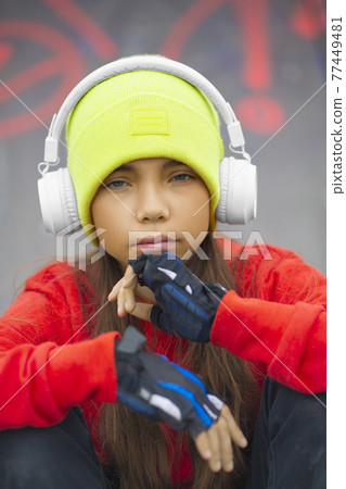 Outdoor portrait of a nine-year-old girl in headphones close-up. She is preoccupied with the issues of growing up and self-determination. 77449481