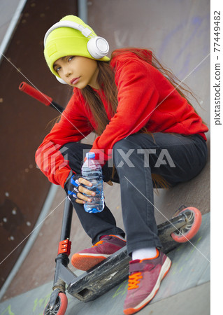 Teenager girl is resting after riding a scooter. Teenager girl is resting after riding a scooter. 77449482