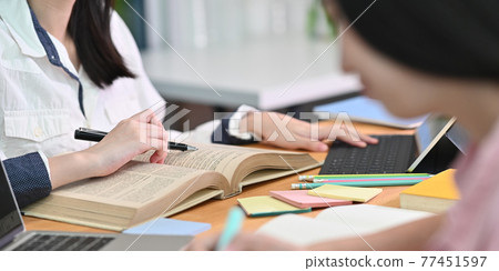 Cropped image of young woman tutoring her lesson while sitting in front her book and computer tablet with keyboard case that putting on cluttered working desk over comfort living room as background. Cropped image of young woman tutoring her lesson while sitting in front her book and computer tablet with keyboard case that putting on cluttered working desk over comfort living room as background. 77451597