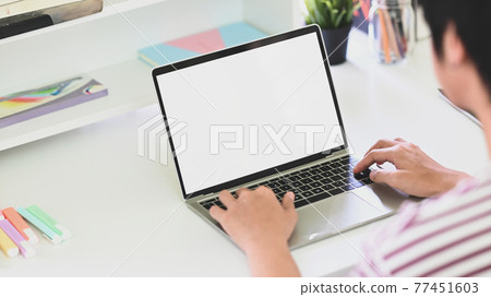 Behind shot of creative man typing on white blank screen computer laptop that putting on white working desk in comfortable living room. Work from home and remote working concept. 77451603