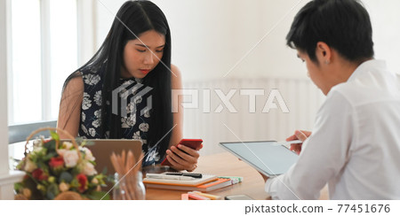 Photo of young couple relaxing and working with computer tablet while sitting together at the wooden working desk over comfortable living room as background. Photo of young couple relaxing and working with computer tablet while sitting together at the wooden working desk over comfortable living room as background. 77451676