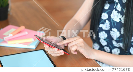 Cropped image of beautiful woman using a smartphone while sitting in front her computer tablet with white blank screen that putting on wooden working desk and surrounded by notebook and marker pens. Cropped image of beautiful woman using a smartphone while sitting in front her computer tablet with white blank screen that putting on wooden working desk and surrounded by notebook and marker pens. 77451678