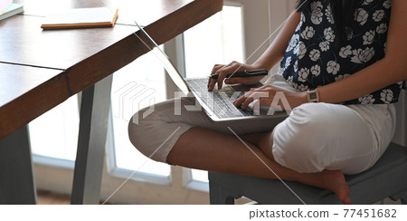 Cropped image of beautiful woman typing on computer laptop that putting on her lap while sitting at the wooden working desk over comfortable living room as background. Cropped image of beautiful woman typing on computer laptop that putting on her lap while sitting at the wooden working desk over comfortable living room as background. 77451682