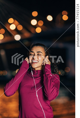 Female runner listening to music on earphones at night Female runner listening to music on earphones at night 77455314