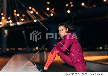 Woman stretching before an evening run. Young female jogger warming up legs at night. Woman stretching before an evening run. Young female jogger warming up legs at night. 77455315