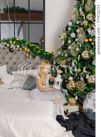 Beautiful little girl sitting by a Christmas tree Beautiful little girl sitting by a Christmas tree 77458255