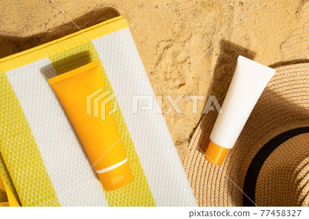 Orange and white tubes of sunscreen on beach next to straw hat and mat. Sun protection on vacation. Top view Orange and white tubes of sunscreen on beach next to straw hat and mat. Sun protection on vacation. Top view 77458327