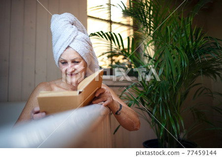 Happy senior woman reading book in bath tub at home. 77459144