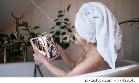 Senior woman with tablet in bath tub at home, video call with daughter and grandchildren. Senior woman with tablet in bath tub at home, video call with daughter and grandchildren. 77459145