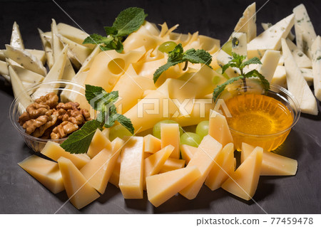 assorted cheese on black slate, nuts and honey, decorated with grapes and mint leaves assorted cheese on black slate, nuts and honey, decorated with grapes and mint leaves 77459478