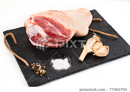 raw pork knuckle with garlic, salt and spices on black stone cutting board.  77460704