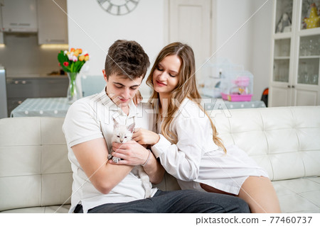 A beautiful couple of young lovers holding a small white kitten. A beautiful couple of young lovers holding a small white kitten. 77460737