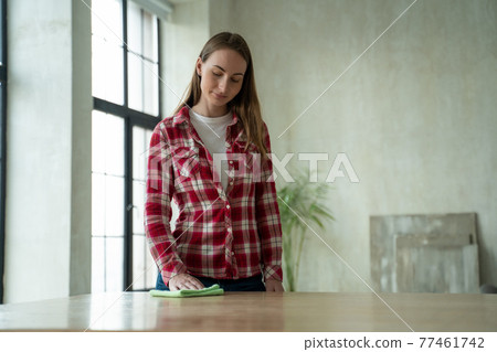 Young woman wipes a table with a rag at home. Concept of homework and household management 77461742