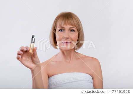 Beauty routine procedures. Sensual mature woman showing bottle with anti-aging serum on light studio background Beauty routine procedures. Sensual mature woman showing bottle with anti-aging serum on light studio background 77461908