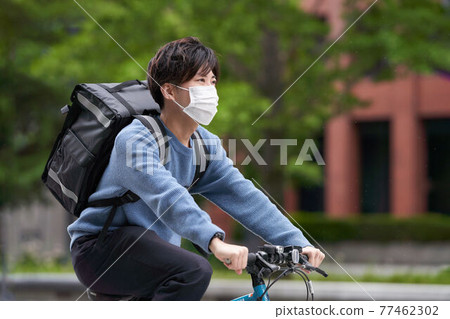 A deliveryman in a mask who runs on a bicycle A deliveryman in a mask who runs on a bicycle 77462302