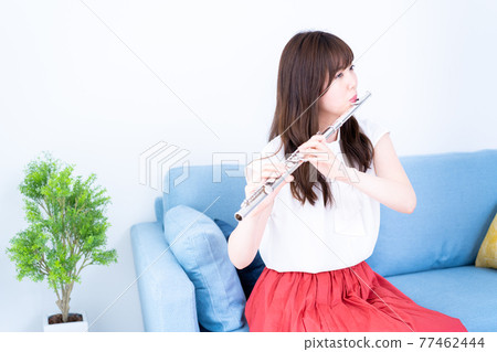 Woman playing the flute on the sofa 77462444