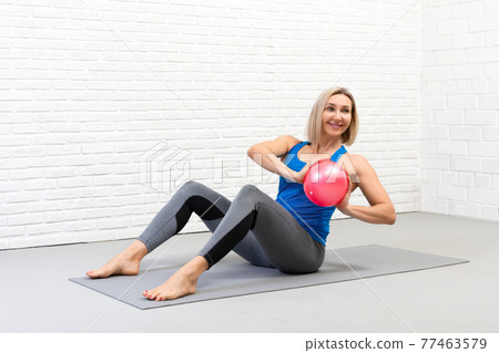 Sitting spine twisting with small fit ball. Attractive adult caucasian woman in sportswear practice pilates indoor. Sitting spine twisting with small fit ball. Attractive adult caucasian woman in sportswear practice pilates indoor. 77463579