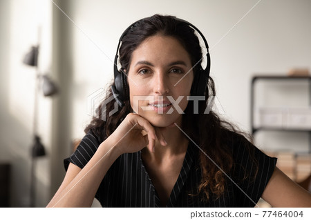 Millennial hispanic woman in wireless headphones telemarketer looking at camera Millennial hispanic woman in wireless headphones telemarketer looking at camera 77464004