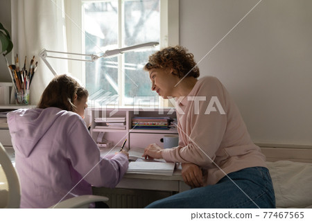 Focused young mother helping teen daughter with homework. 77467565