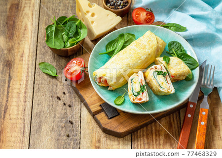 Japanese cuisine. National Japanese dish Omelet tamago yaki for breakfast. Rolled egg with spinach, tomato and cheese on a wooden table. Copy space. Japanese cuisine. National Japanese dish Omelet tamago yaki for breakfast. Rolled egg with spinach, tomato and cheese on a wooden table. Copy space. 77468329