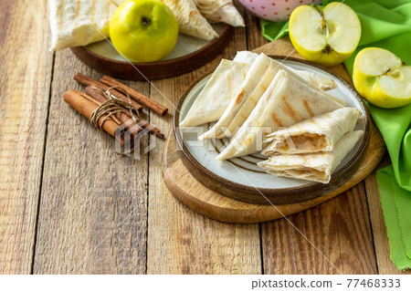 Apple pastries for breakfast. Grilled lavash triangle with apples and cinnamon on a wooden wooden table. Copy space. Apple pastries for breakfast. Grilled lavash triangle with apples and cinnamon on a wooden wooden table. Copy space. 77468333