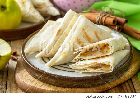 Apple pastries for breakfast. Grilled lavash triangle with apples and cinnamon on a wooden wooden table. Apple pastries for breakfast. Grilled lavash triangle with apples and cinnamon on a wooden wooden table. 77468334