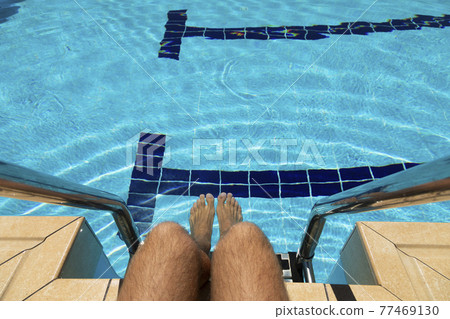 The feet of a young man in a swimming pool in summer, Spain. 77469130